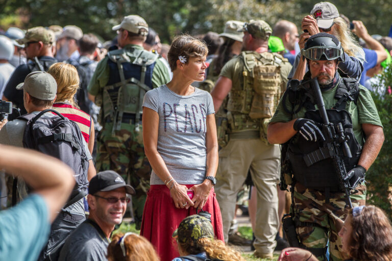 Photo of hippy-like woman in peace t-shirt next to soldier in camo holding gun
